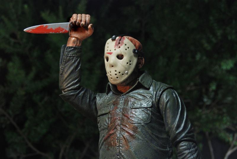 A person in a hockey mask and green jacket wields a bloodied knife among trees, evoking a horror scene like the NECA Friday the 13th Part IV: The Final Chapter Jason Voorhees Ultimate Action Figure (7 inch).