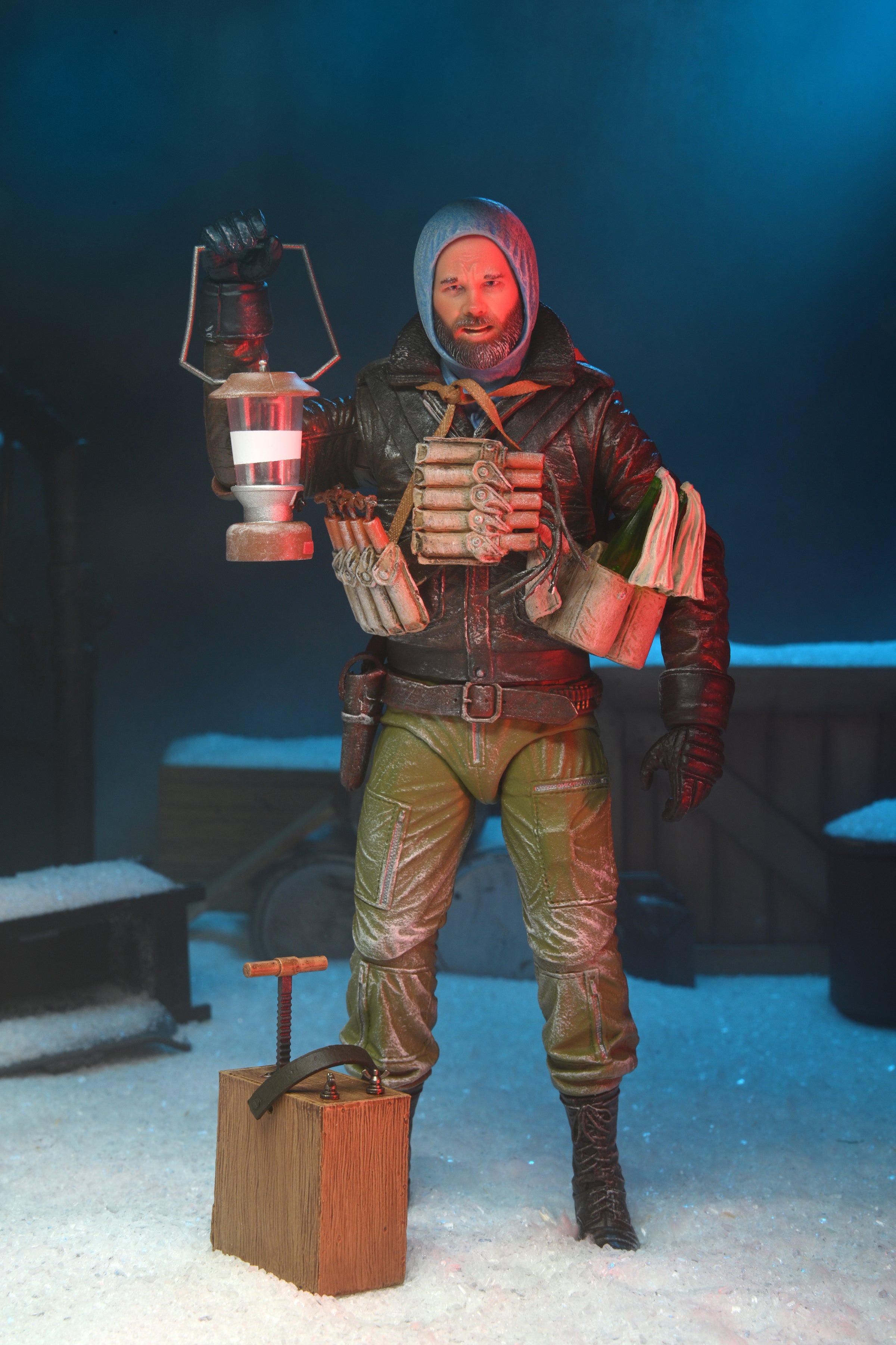 The NECA The Thing R.J. MacReady Last Stand Ultimate Action Figure (7 inch) features MacReady in a hooded jacket and green pants, holding a lantern with dynamite on his chest, set amid snowy terrain and industrial crates in the background.