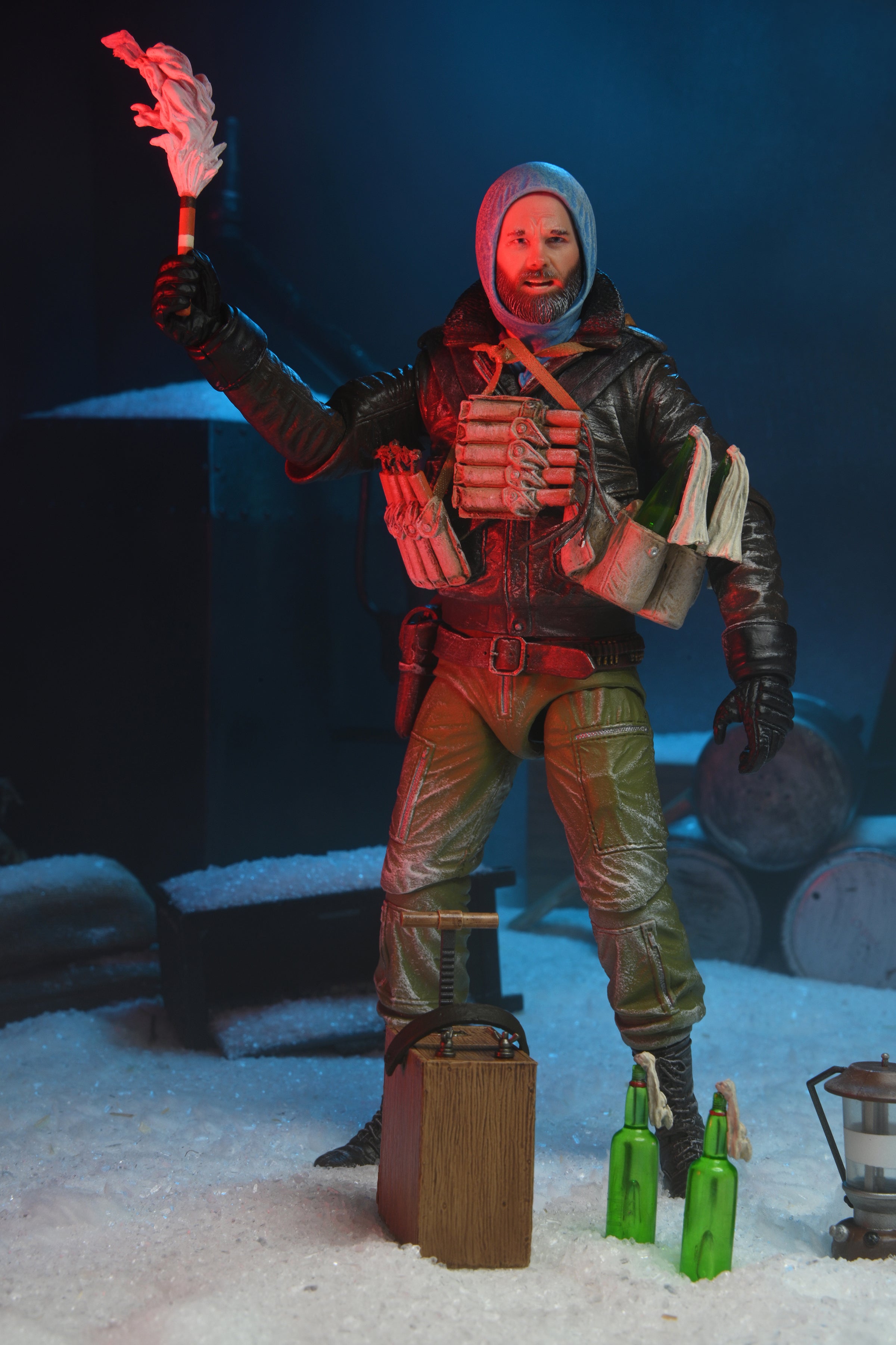 The NECA The Thing R.J. MacReady Last Stand Ultimate Action Figure (7 inch) stands in winter gear with a torch, surrounded by snow, bottles, a wooden box, and barrels in blue light—a must-have for any Kurt Russell or The Thing collection.