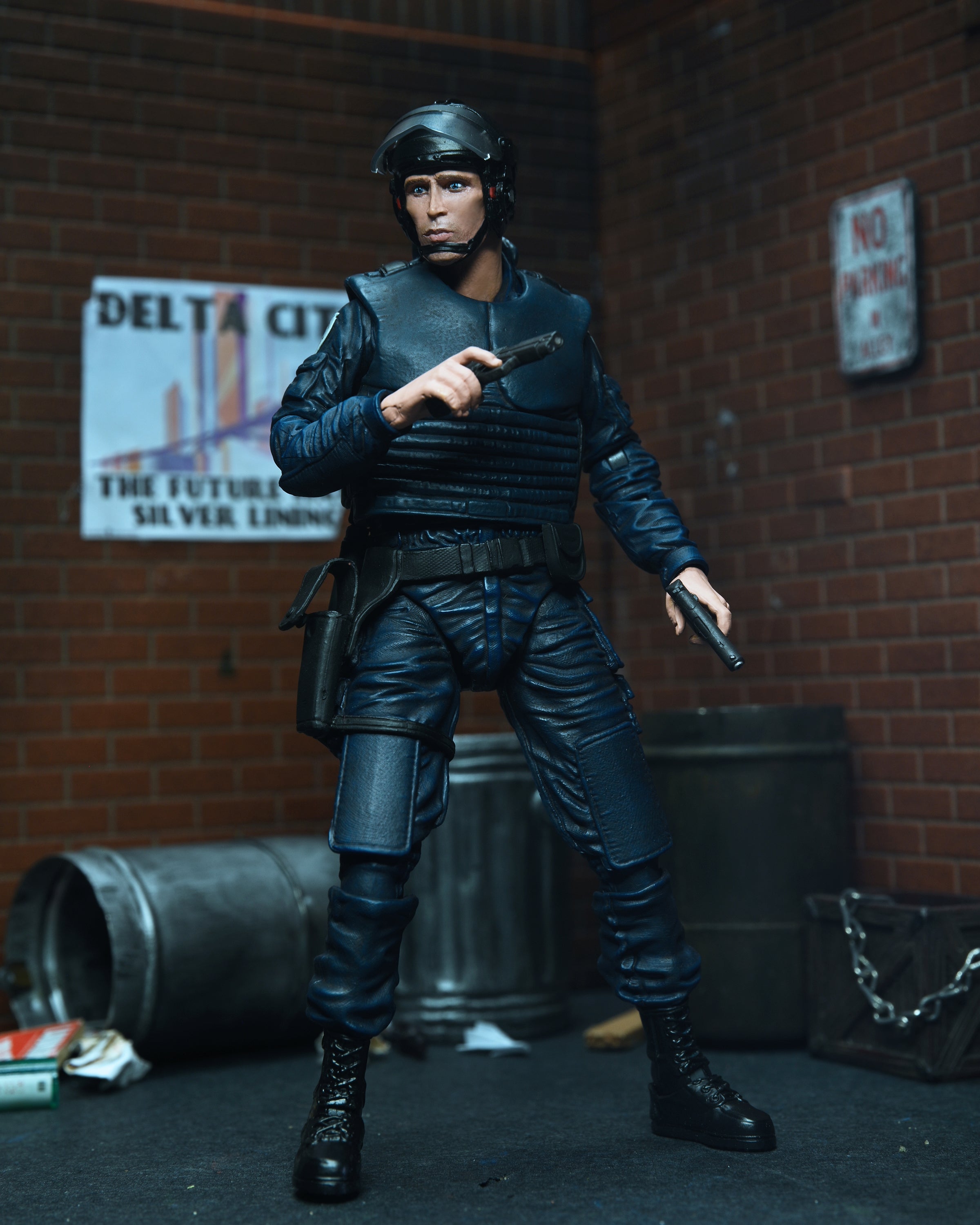 The NECA RoboCop Alex Murphy OCP Uniform Ultimate Action Figure (7 inch) features Alex Murphy in his police uniform, holding a gun and baton, posed in an alley scene with brick walls, posters, and a trash can. Brand: NECA.