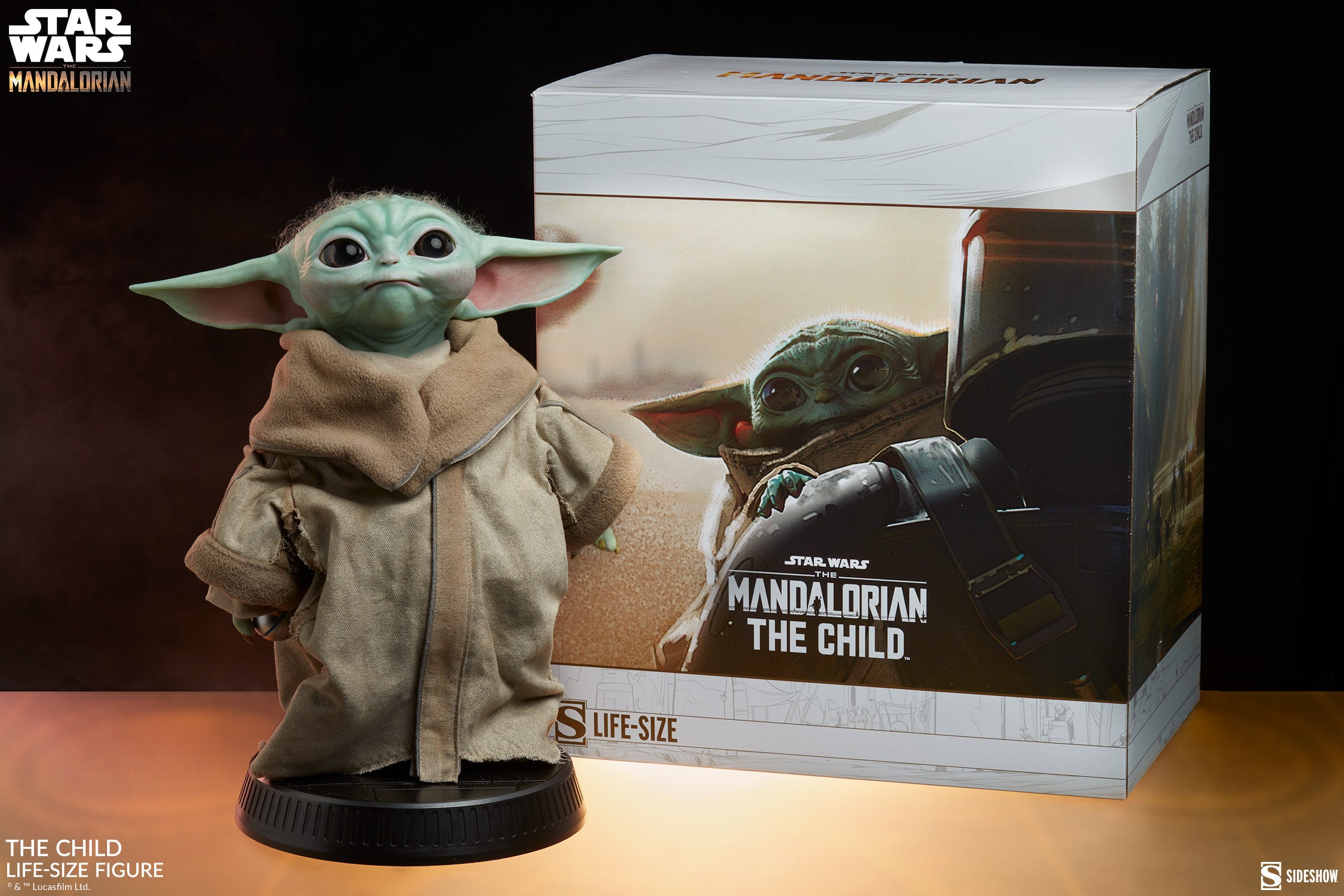 The Sideshow Star Wars: The Mandalorian – The Child Life-Size Figure (1:1 Scale) stands beside its box, featuring the branding. Grogu wears a beige robe, with large ears and expressive eyes capturing Baby Yoda’s iconic charm.